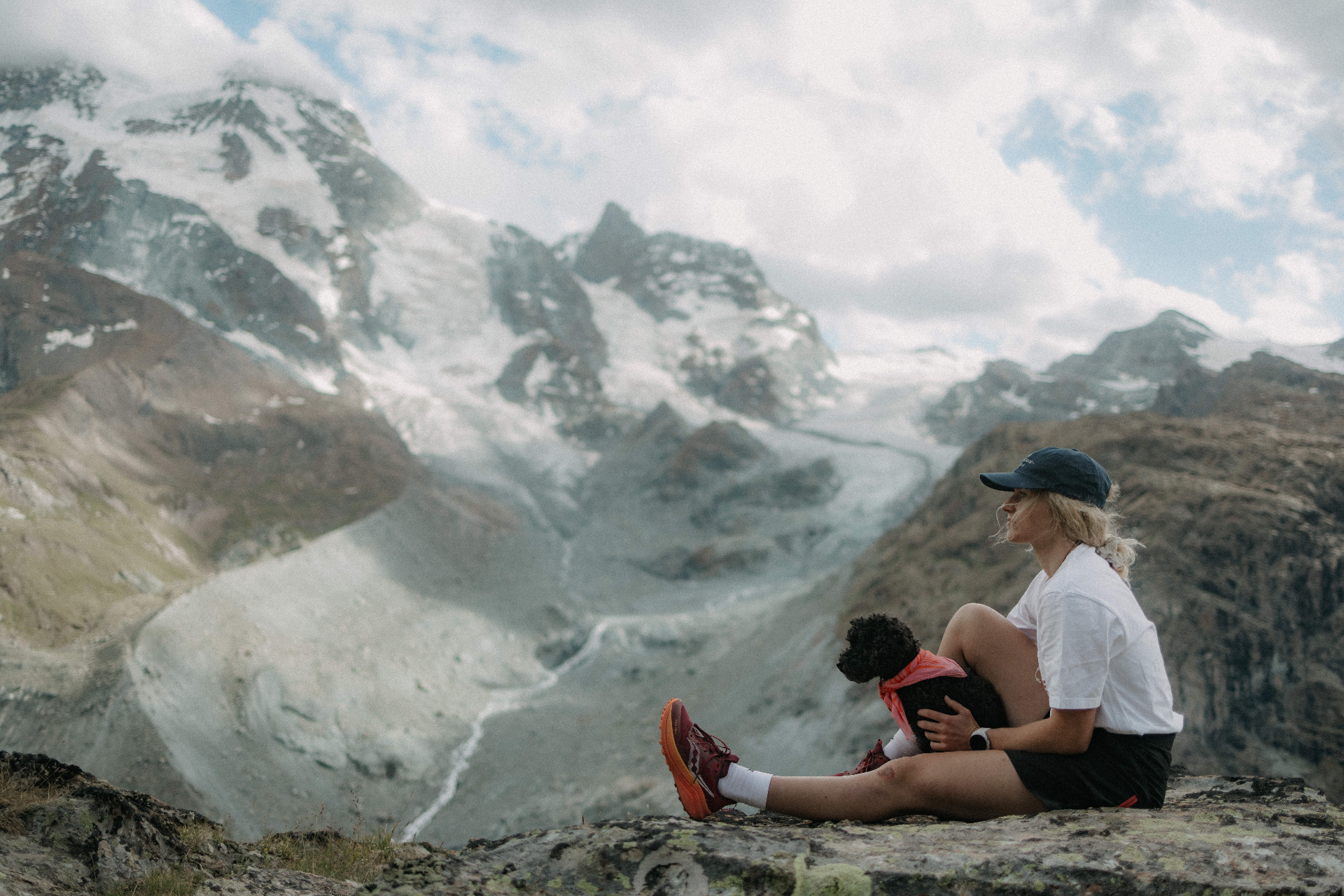 A hiker pauses for rest on a rocky outcrop, looking out over a mountain landscape.