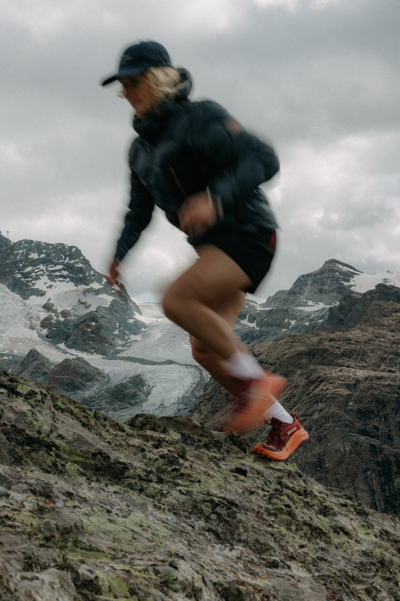 A person running on a narrow trail on a green mountainside.