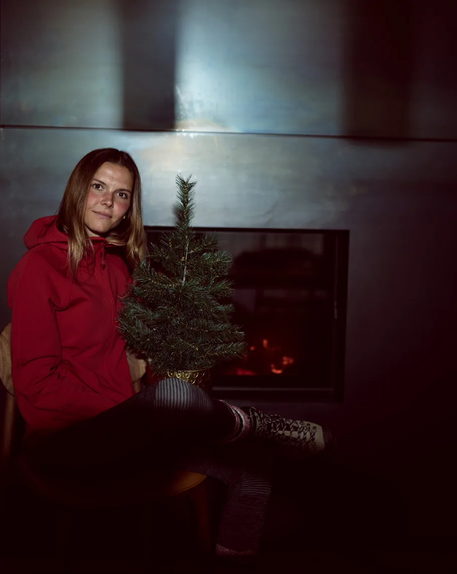A woman in a quiet-luxury red coat beside a fireplace — texture and considered colour, status without advertisement.